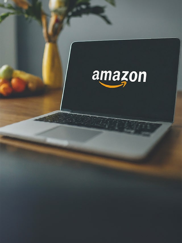 E-commerce giant Amazon with logo on laptop screen with yellow flower pot and fruit plate kept on table; concept of Amazon WoW Internship 2024: Full Details