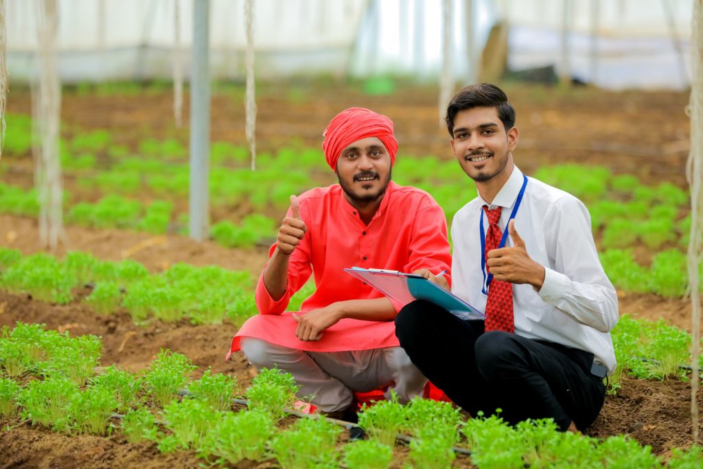 Young SBI intern and farmer showing thumps up at a vegetable farm in a rual setting; concept SBI fellowship program for rural areas